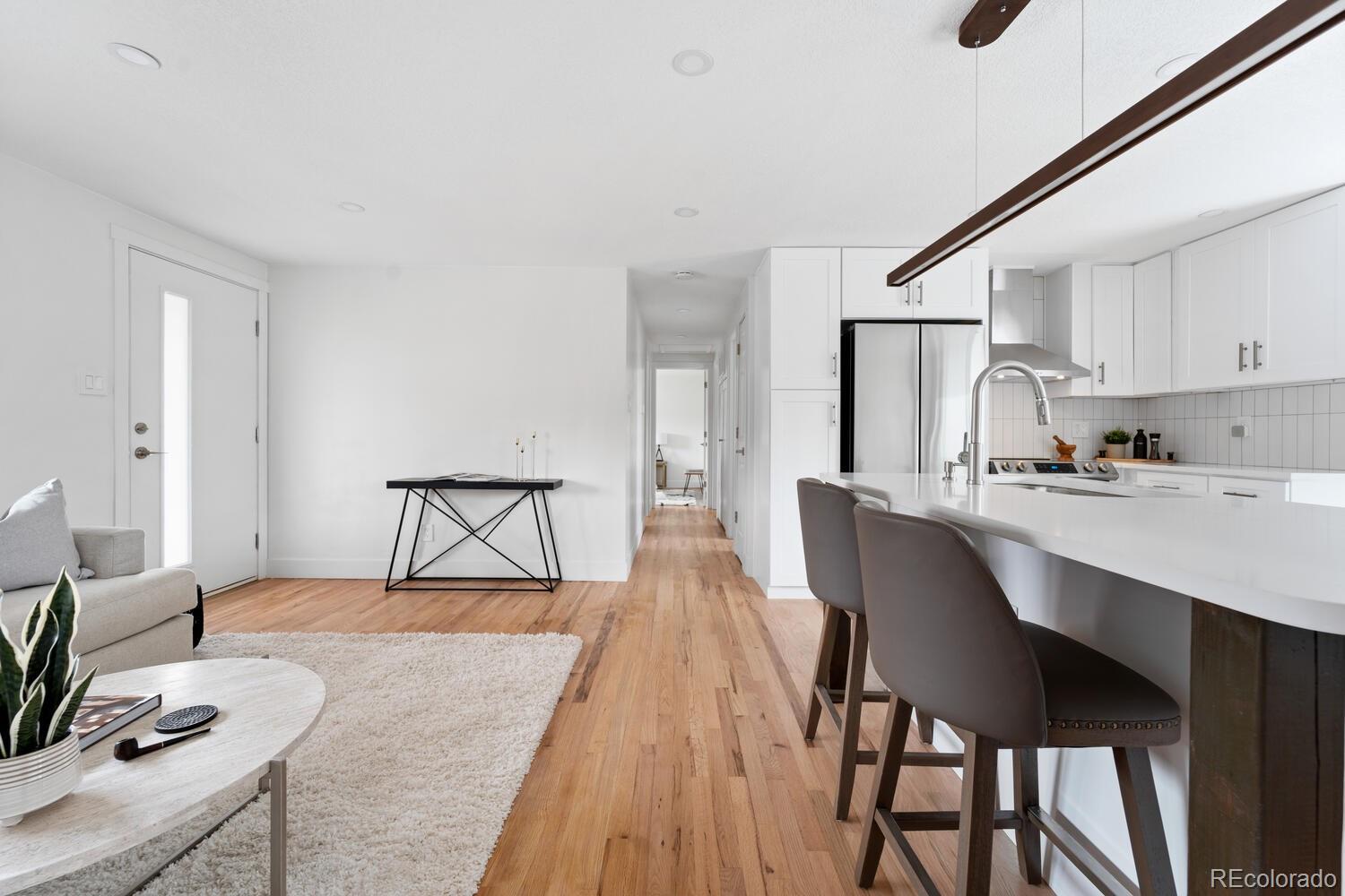 Open-plan kitchen and living room with a white island, bar stools, and light wood floors.