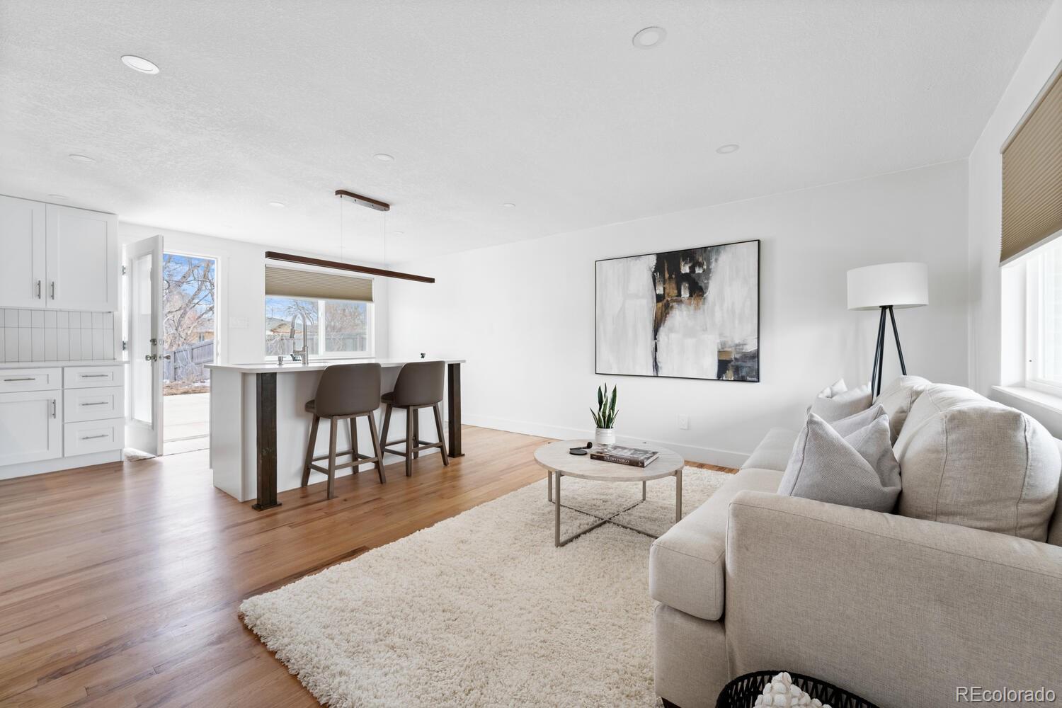 Open-plan living room and kitchen with a large island, light wood floors, and a pale sectional sofa.