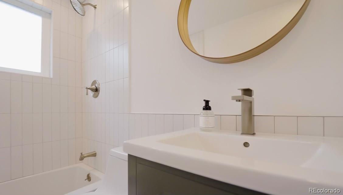 Bathroom vanity with a modern faucet beside a tiled bathtub with brass fixtures.