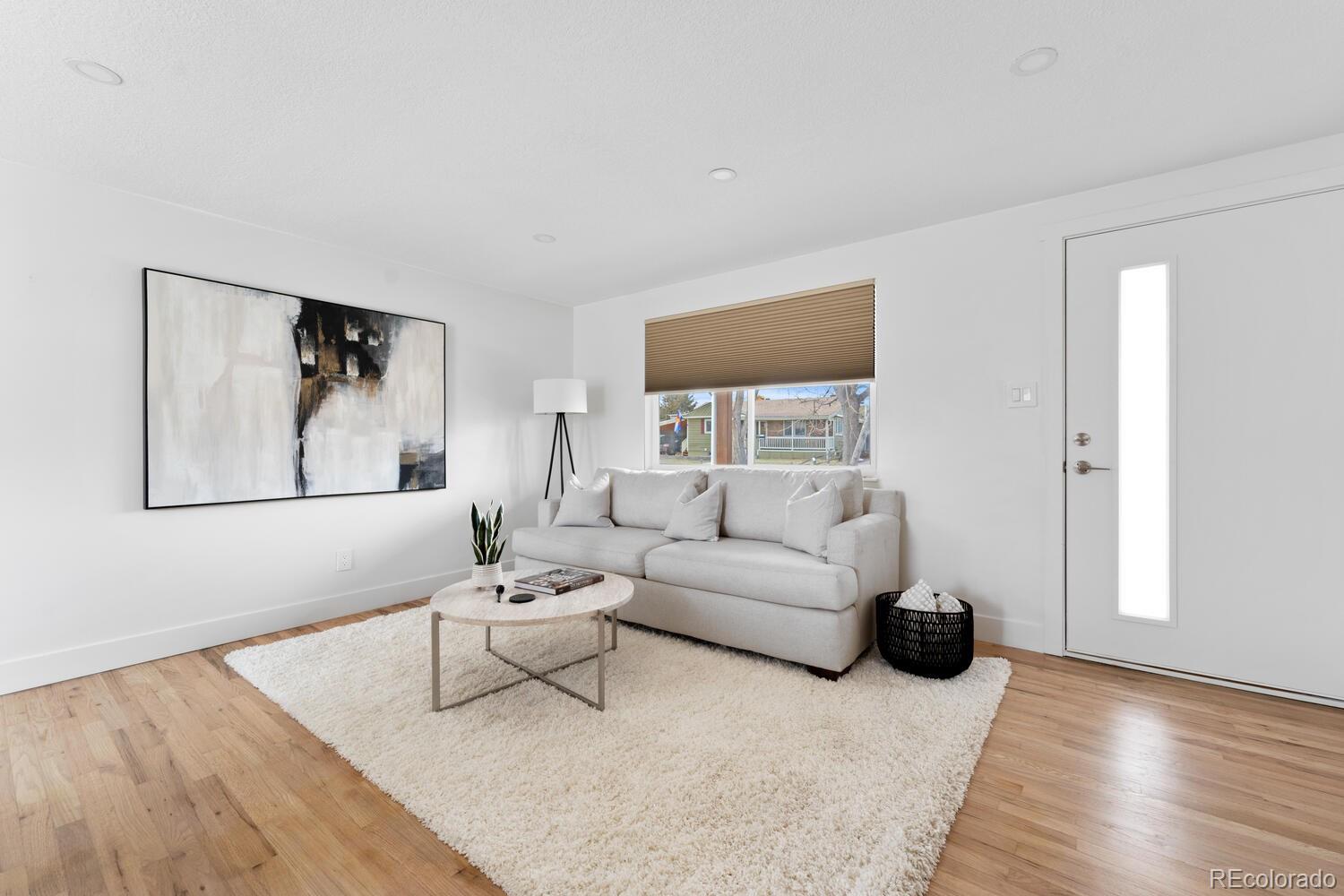Living room with a light gray sofa, round coffee table, abstract wall art, and hardwood floors.