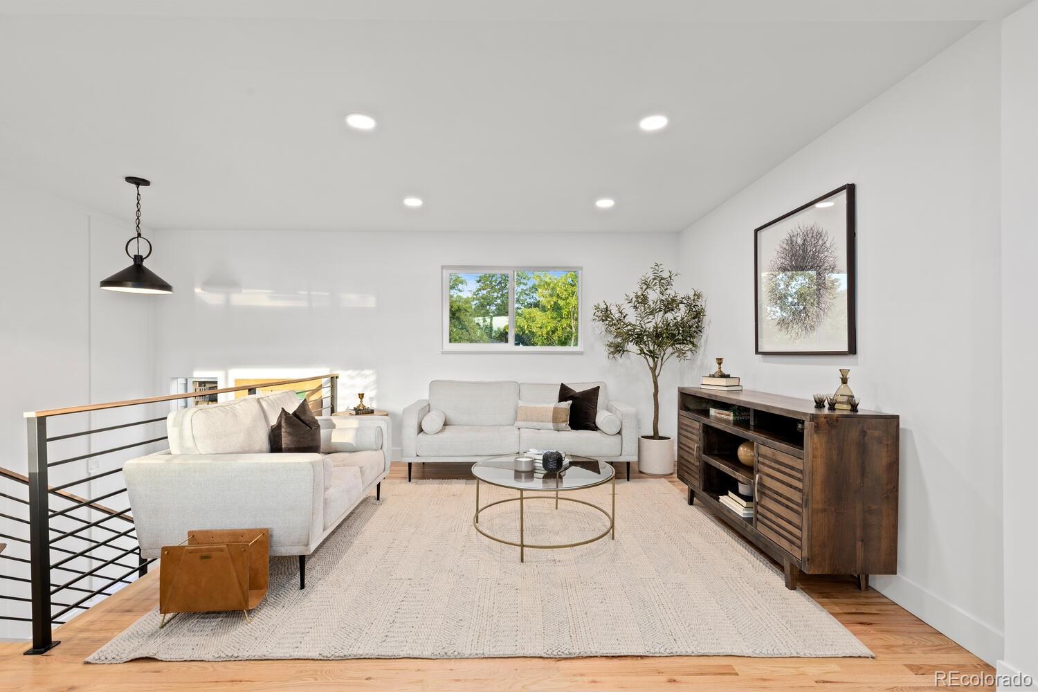 Staged living room with white sofas, a glass coffee table, and a black metal stair railing.