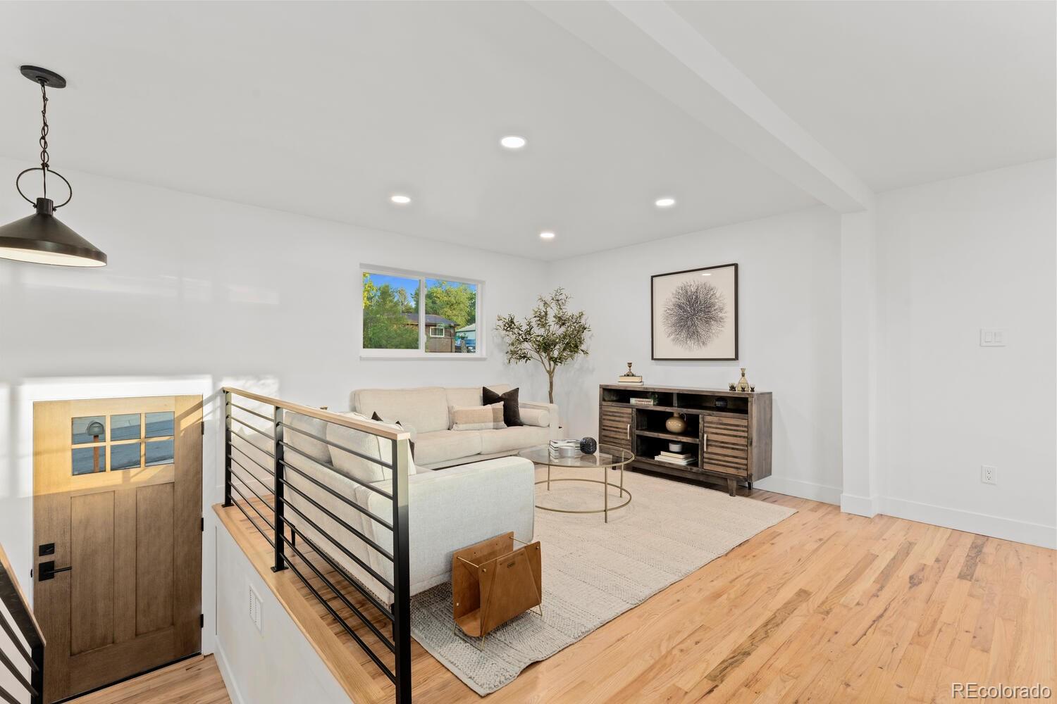 Staged living room with cream sofas, hardwood floors, and a black metal stair railing.
