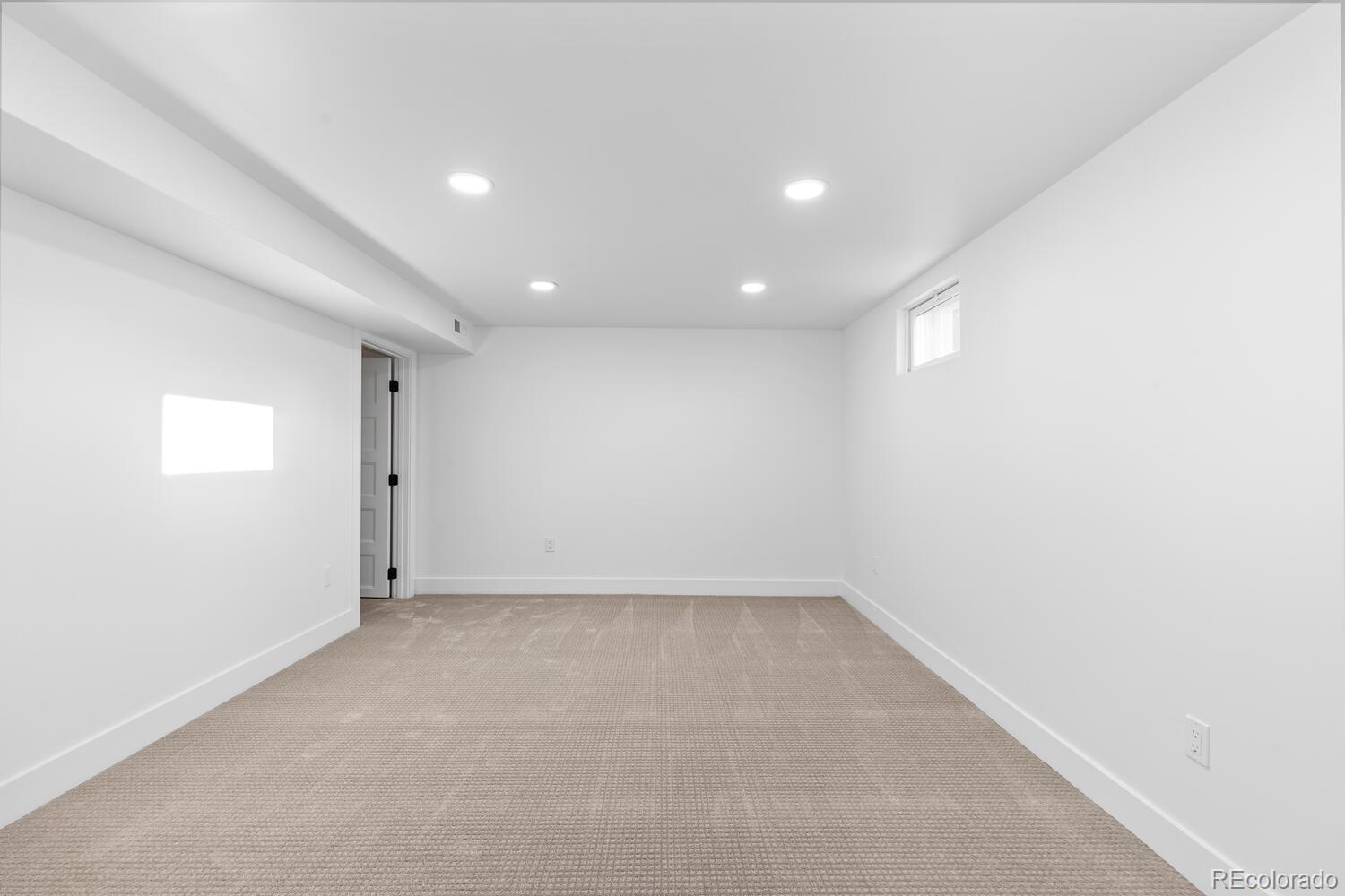 Empty carpeted room with recessed lights and a small high window.