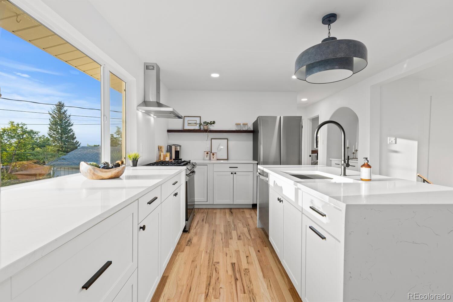 Bright white kitchen with two quartz islands, stainless steel appliances, and large windows overlooking trees.