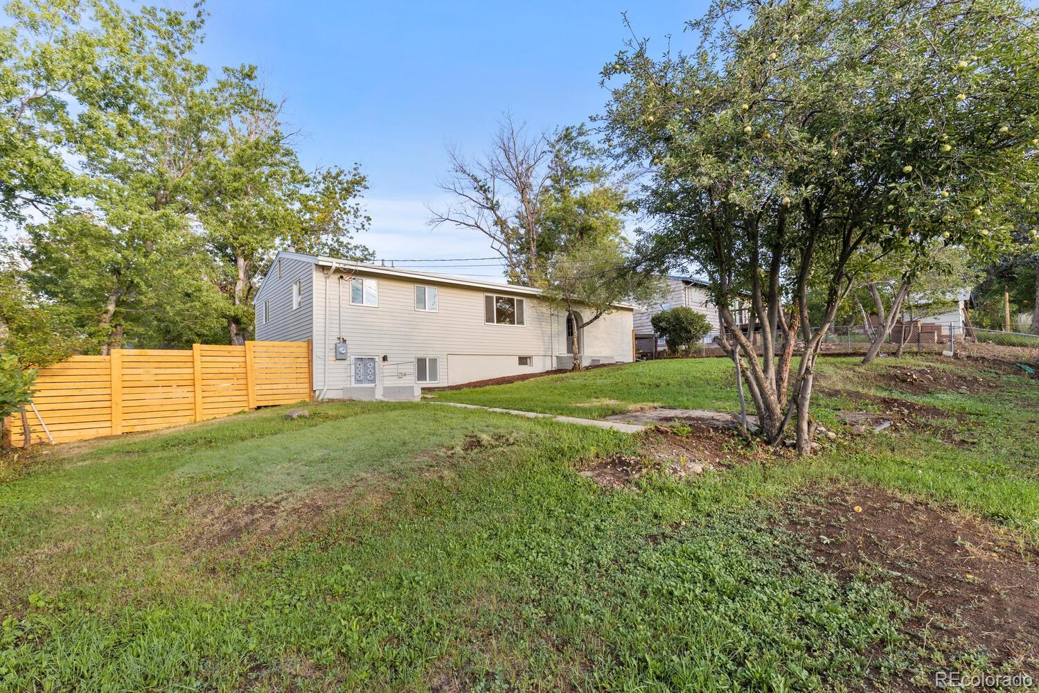 Rear side of a light-colored split-level house above a sloping grassy yard and wooden fence.