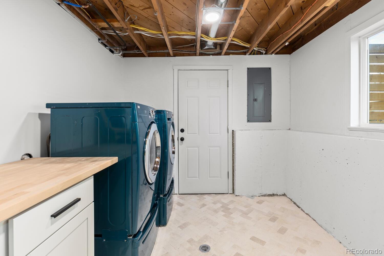 Laundry room with teal washer and dryer beneath an exposed ceiling.