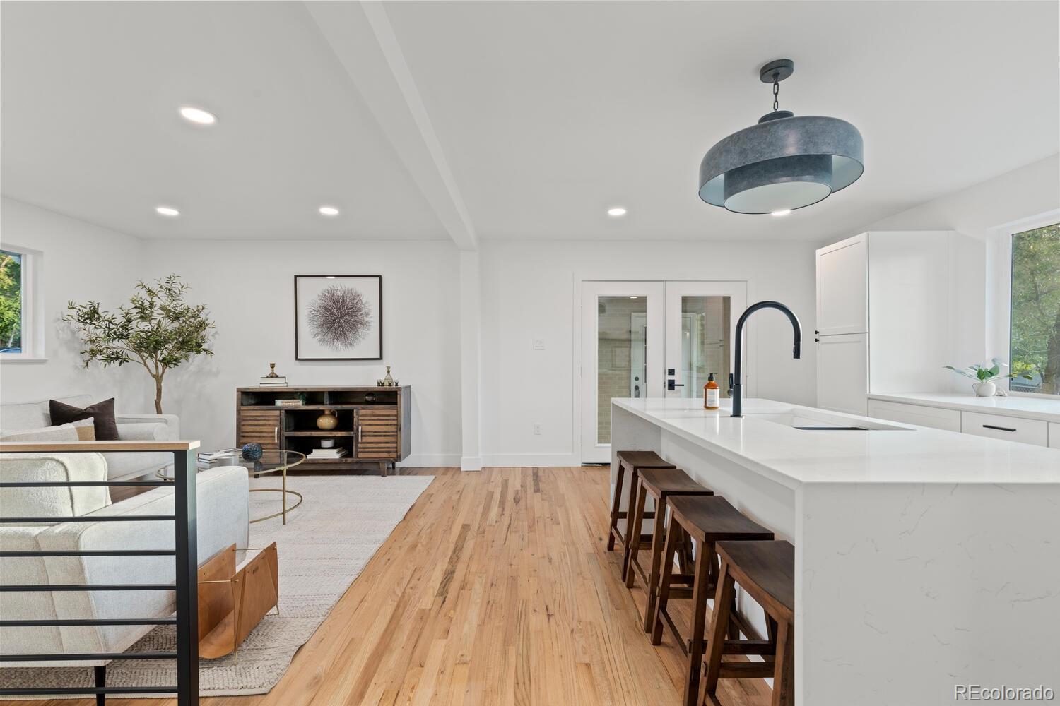 Open kitchen and living area with a long quartz island, dark stools, and light wood floors.