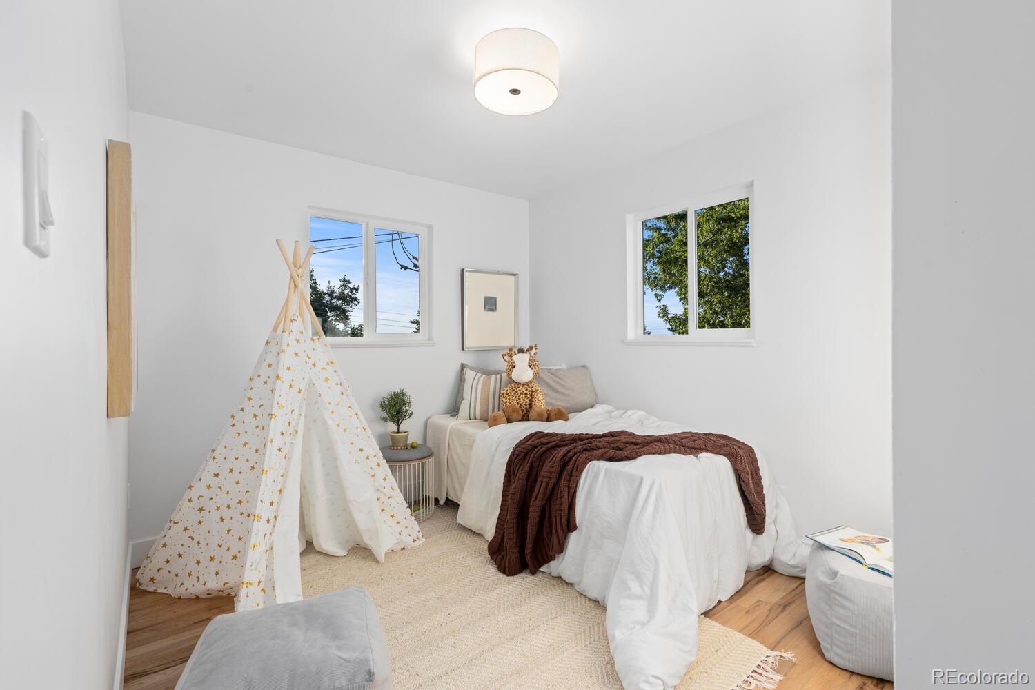 Staged bedroom with a white bed, brown throw, star-patterned teepee, and plush giraffe.