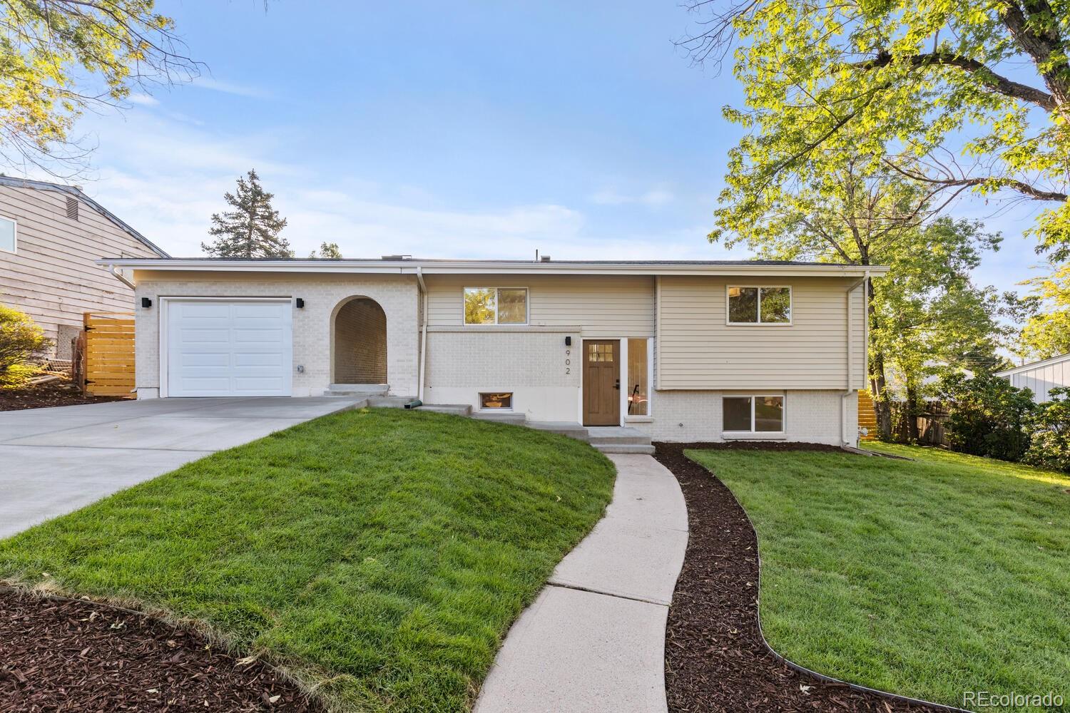 Split-level home with an attached garage, white brick facade, and curved front walkway.