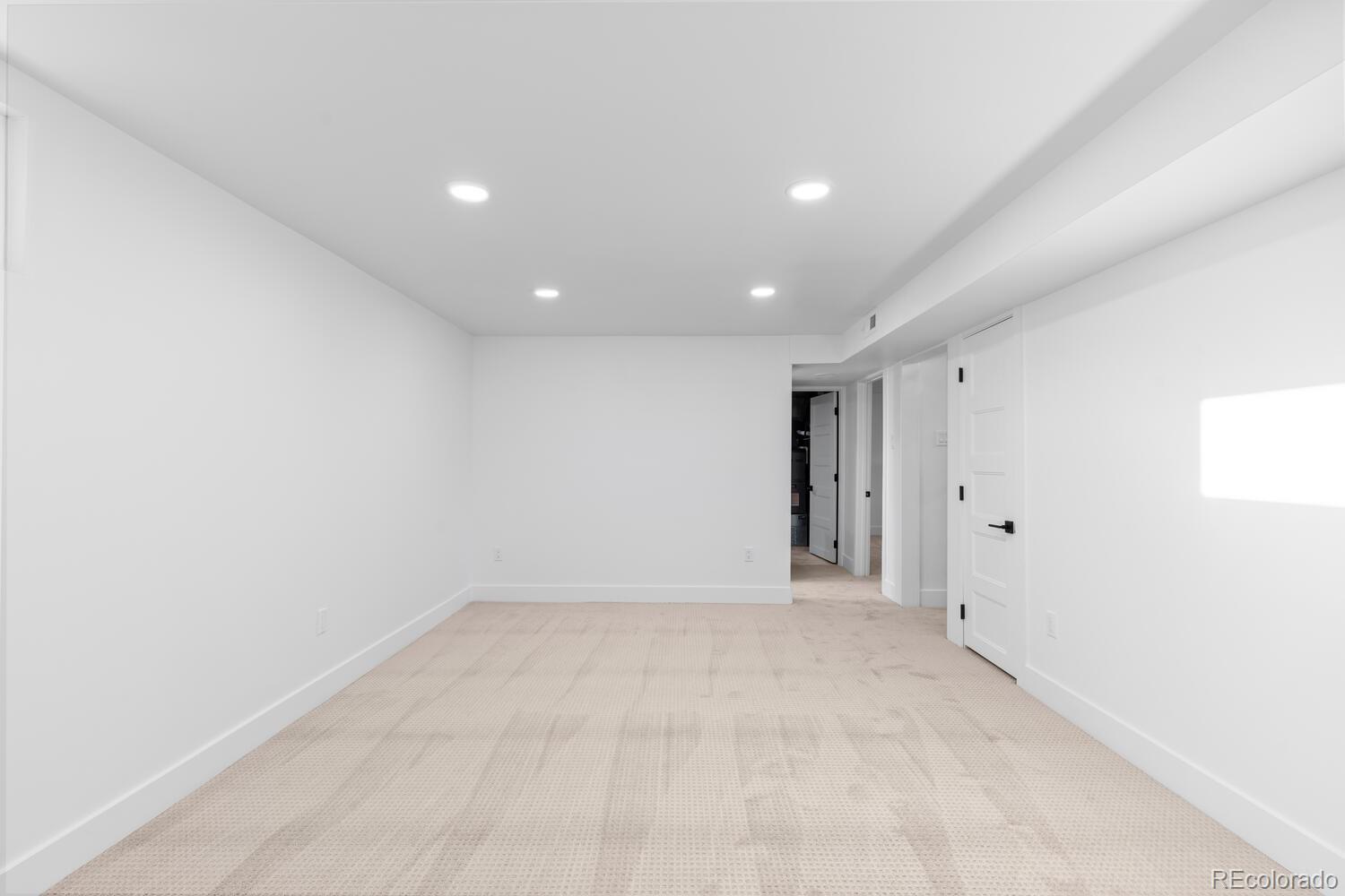 Empty carpeted room with recessed lights and doors to adjoining spaces.