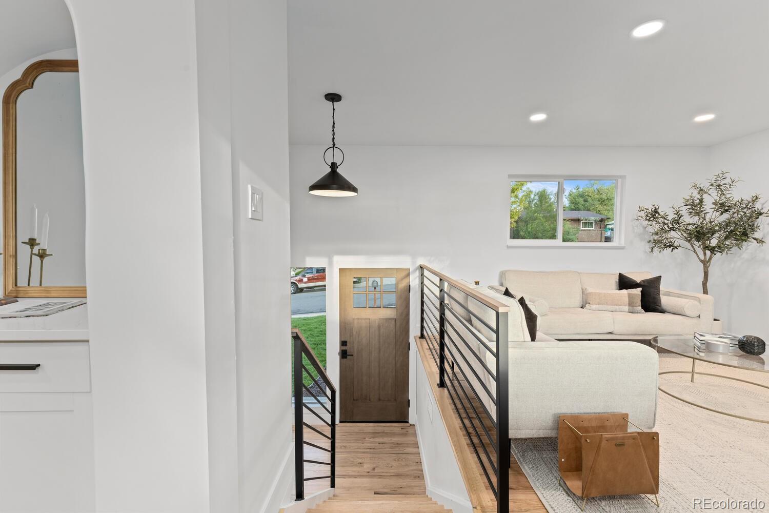 Staged living room overlooking the entry, with a white sectional sofa, wood front door, and open staircase.