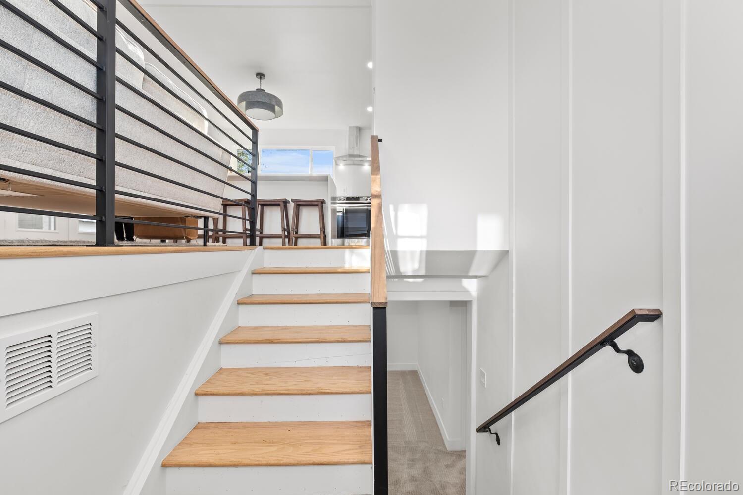 Split-level staircase with wood treads and black railings leading to an open kitchen and loft.