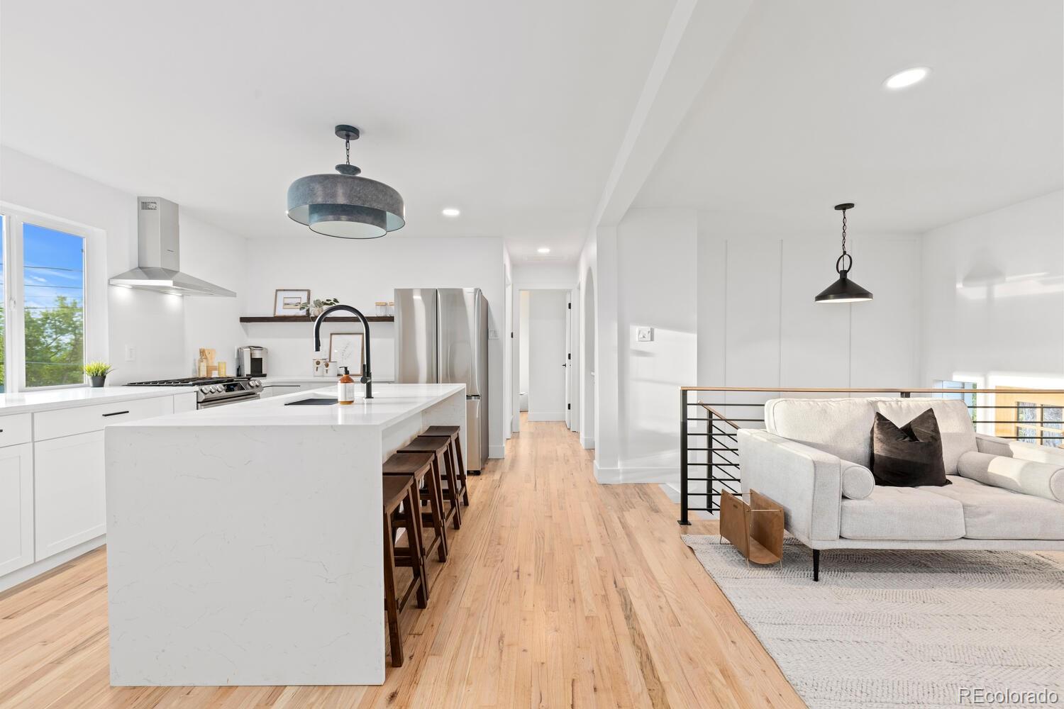 Open-plan kitchen and living area with a waterfall island, wood floors, and white sofa.