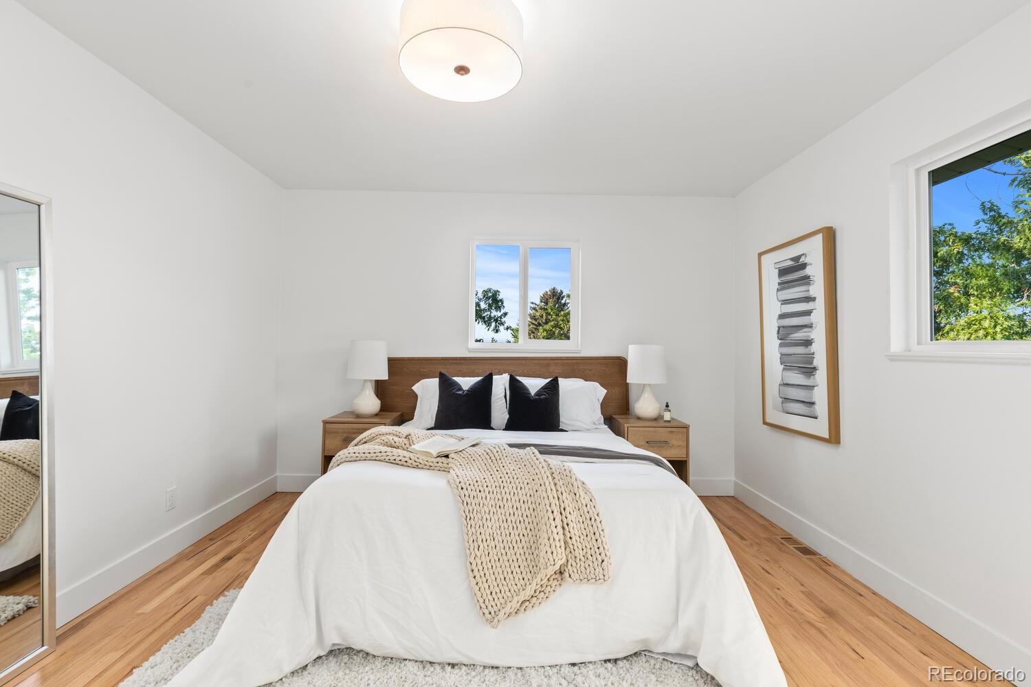 Staged bedroom with a white bed, wood headboard, knitted cream throw, and hardwood floors.