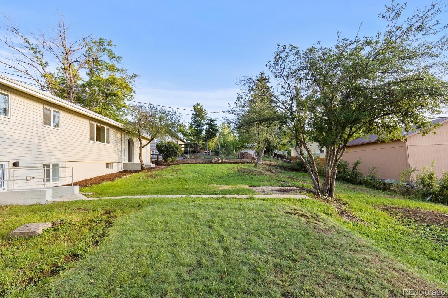 Backyard with a broad grassy lawn, mature trees, and the home’s lower-level patio area.
