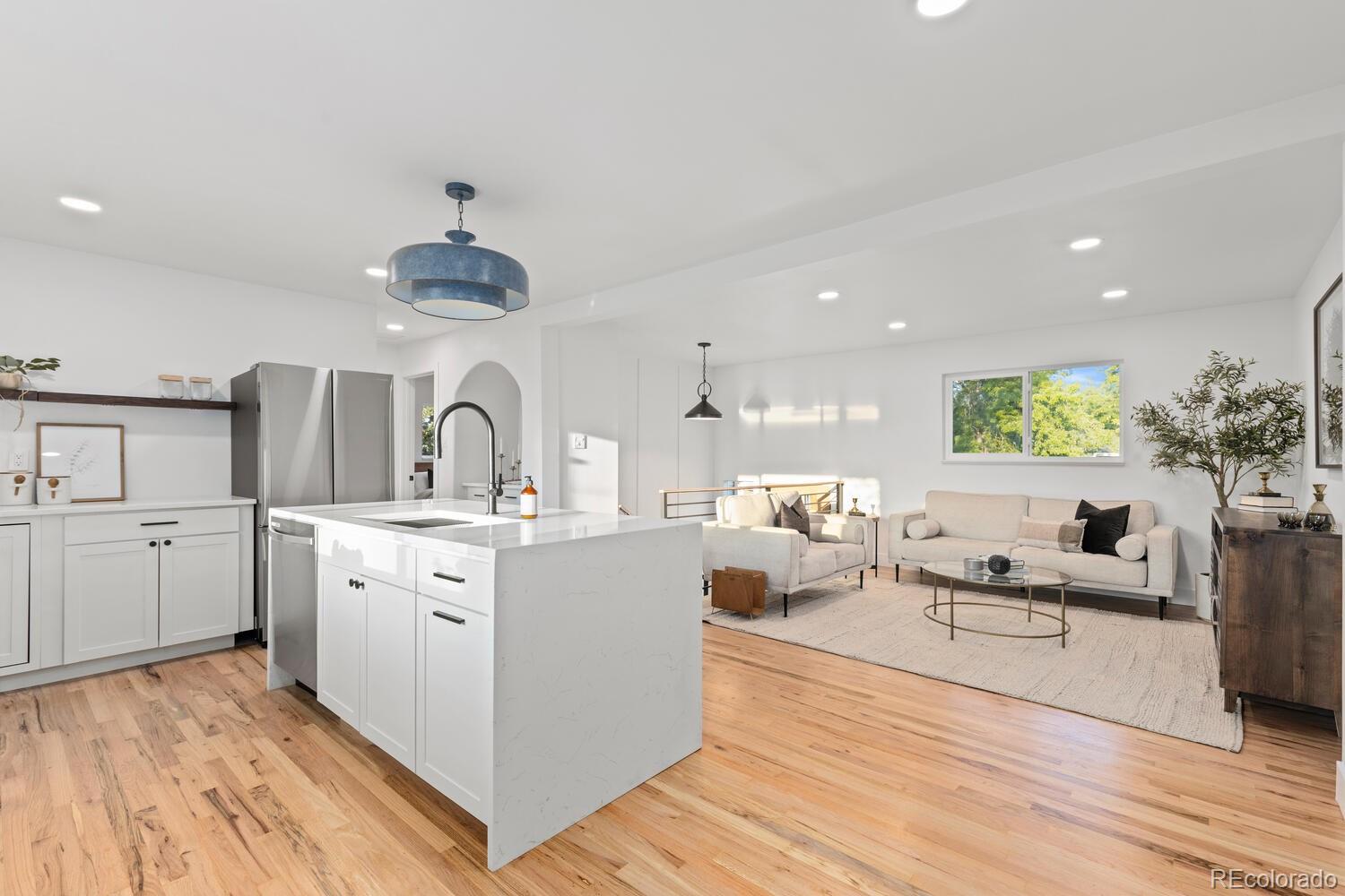 Open-plan kitchen and living room with a large white island and light wood floors.