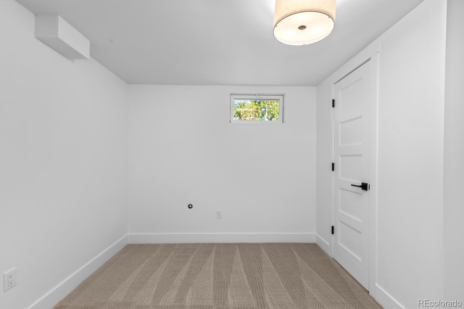 Empty carpeted room with a small high window and white paneled door.