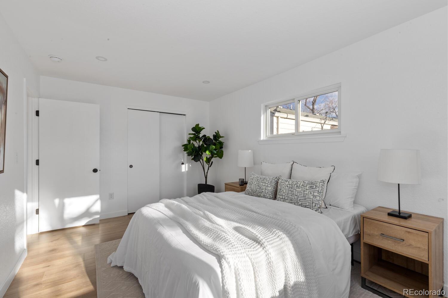 Bright bedroom with a white bed, patterned pillows, wood nightstands, and a high horizontal window.