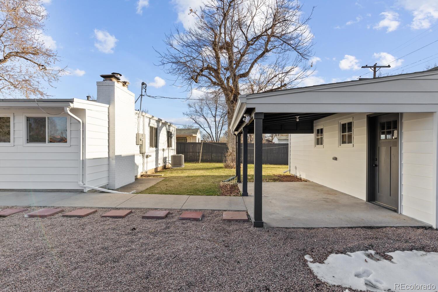 Home’s rear patio with a covered concrete area, gravel yard, and leafless tree.