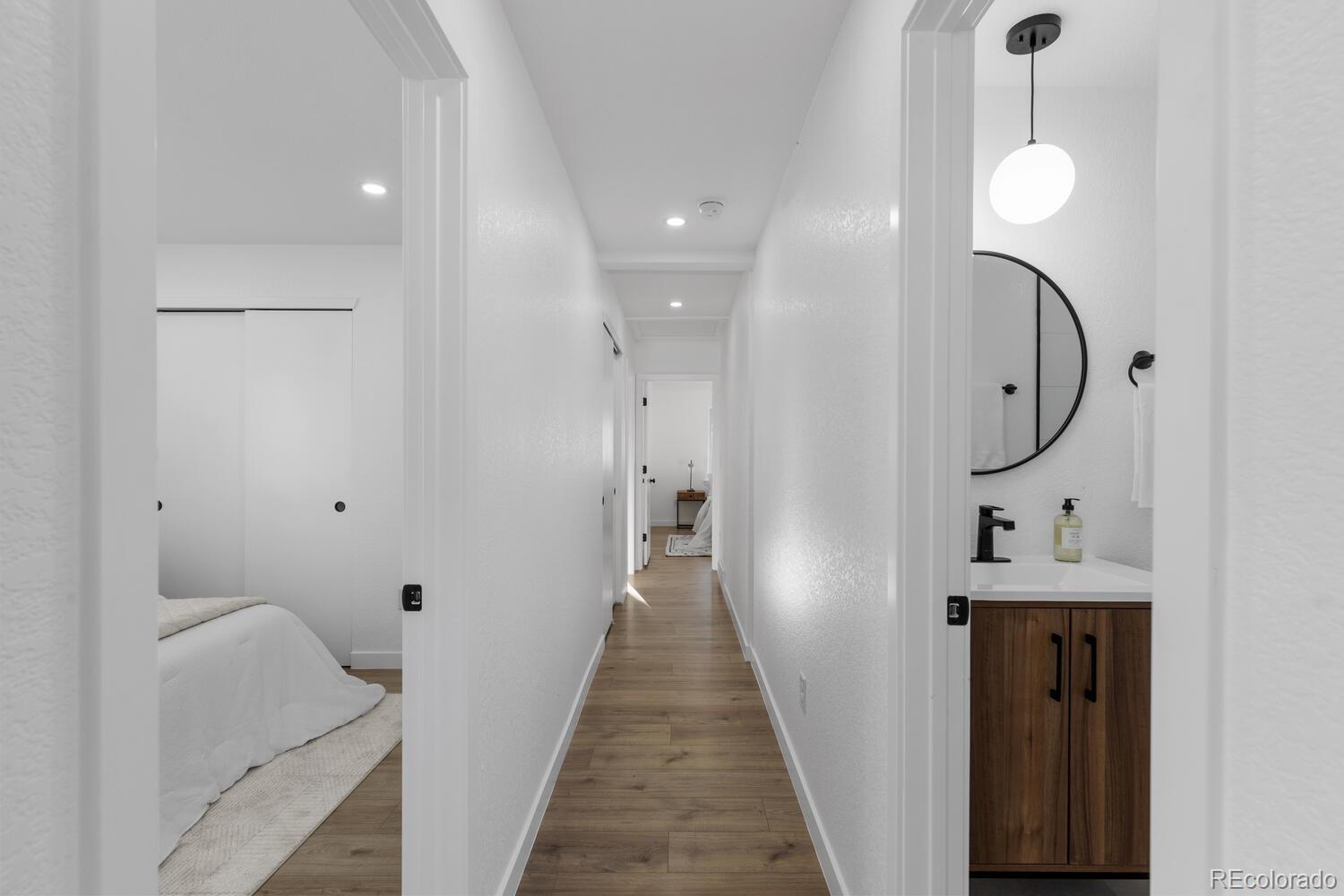Bright hallway with wood-look floors, a bedroom on the left, and a bathroom vanity on the right.