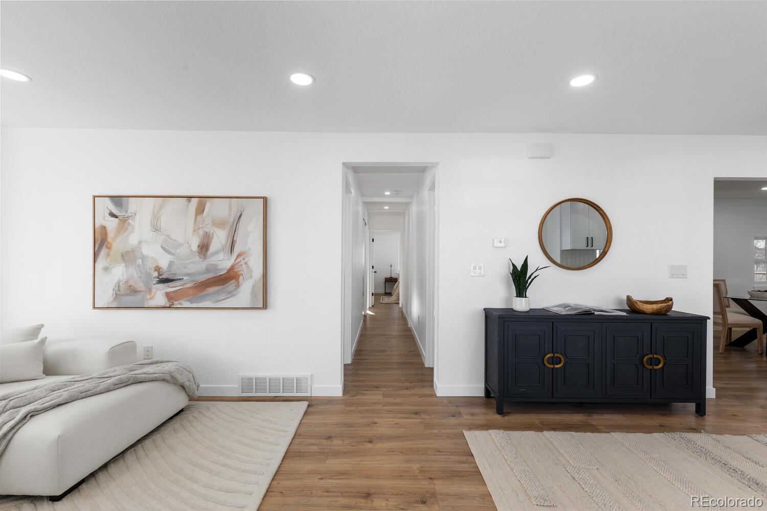 Living room with a white sofa, abstract art, and dark sideboard beside a hallway.