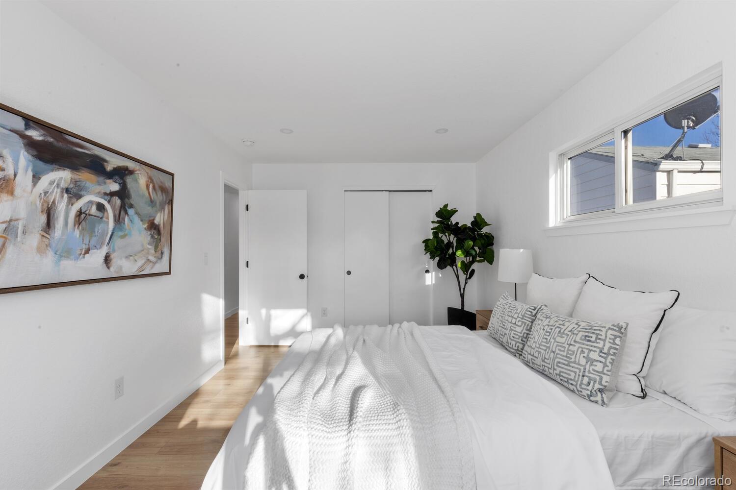 Bright bedroom with a white bed, abstract wall art, and a high horizontal window.