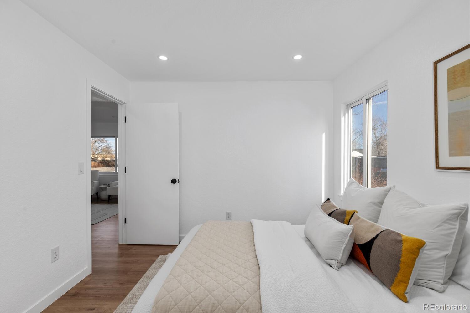 Bright bedroom with white bedding, a large window, and a mustard-yellow accent pillow.