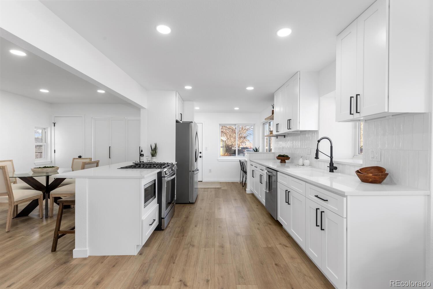 Open kitchen with white cabinets, a large island, stainless steel appliances, and light wood floors.