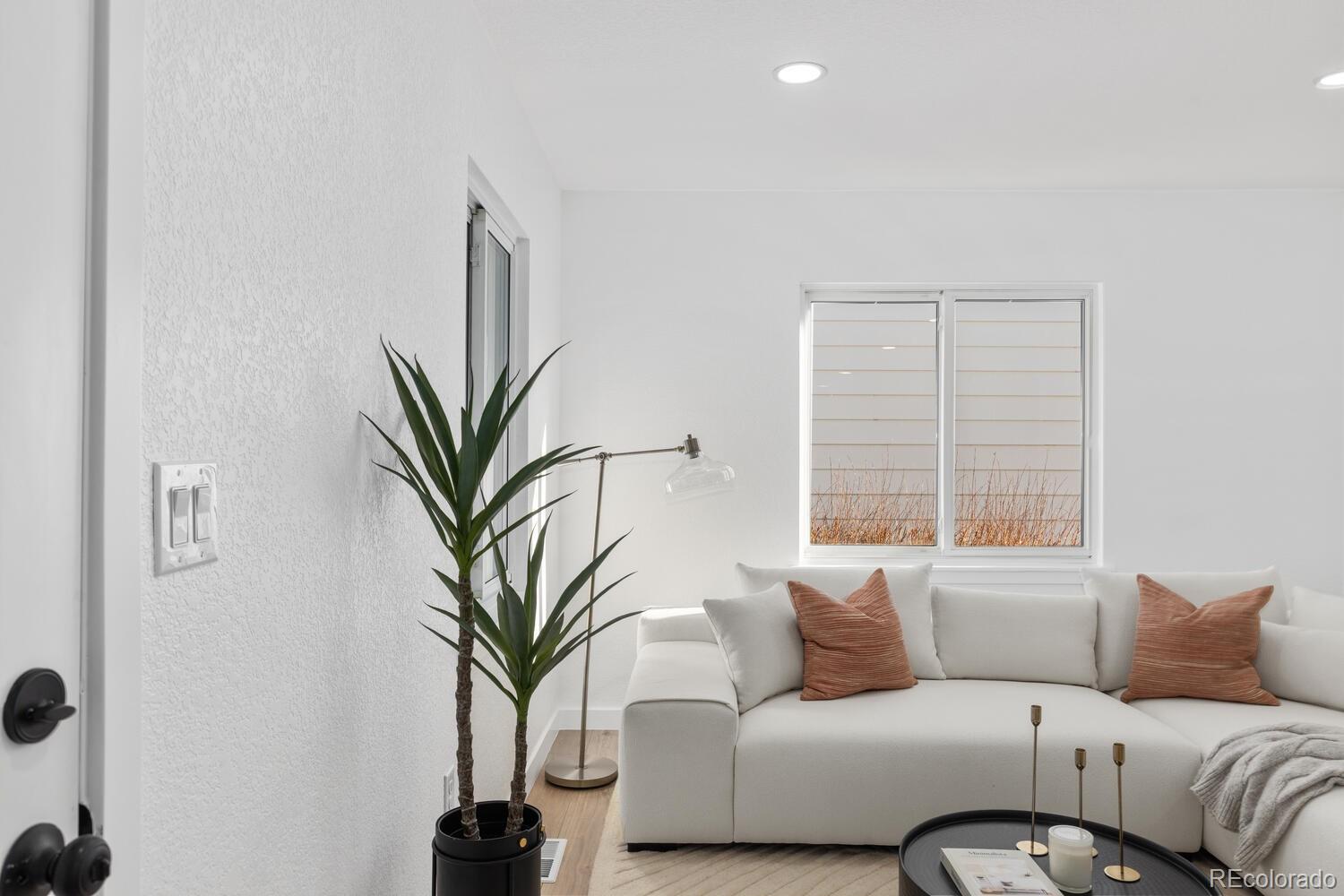 Bright living room with a white sectional, rust-colored pillows, and a tall potted plant.