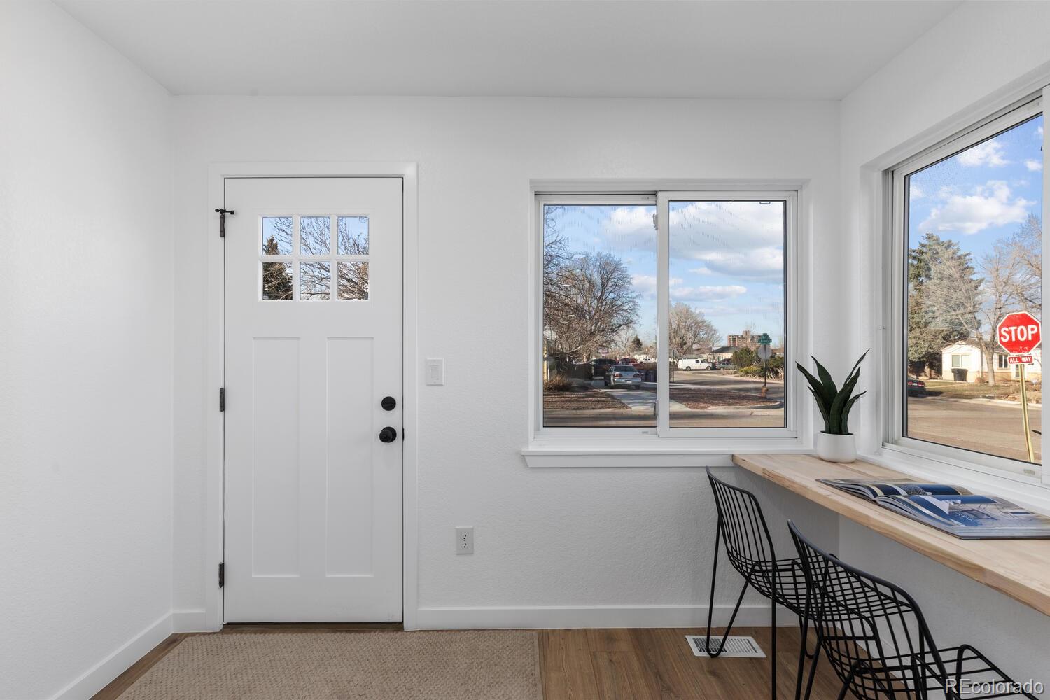 Bright entry room with a white front door, street-facing windows, and a wood counter with black chairs.