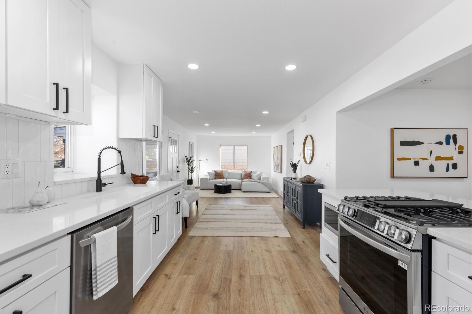 Staged white kitchen with a stainless-steel range opening into a living room.