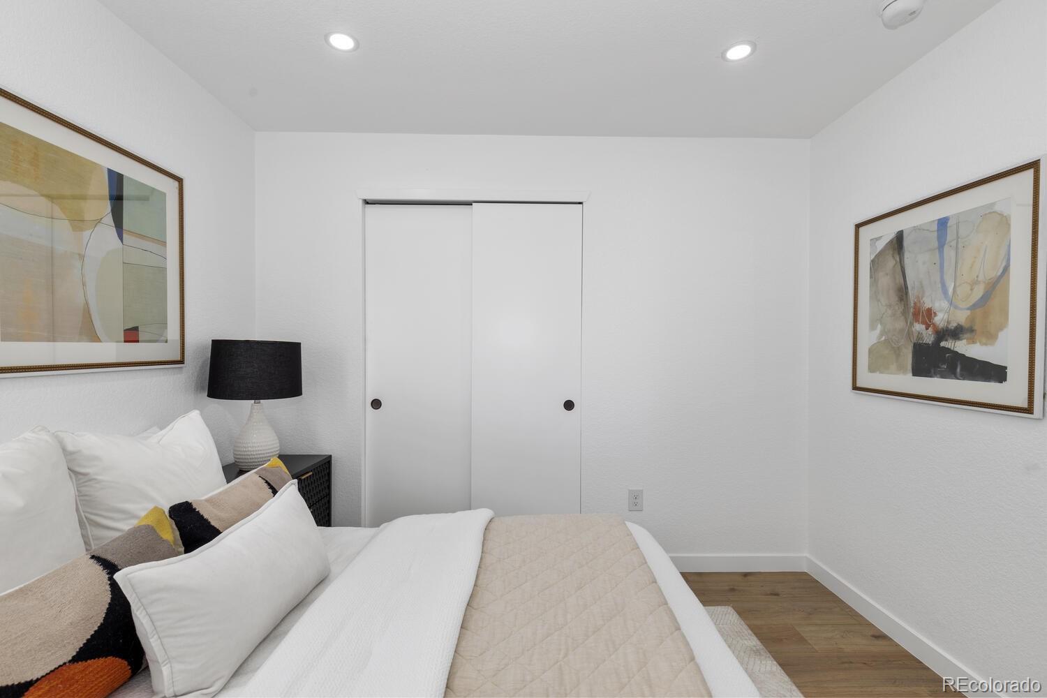 Staged bedroom with a white bed, framed abstract artwork, and sliding closet doors.