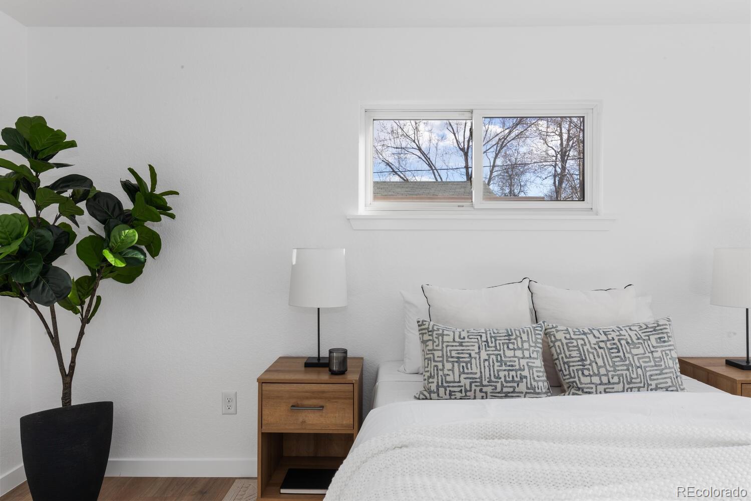 Bedroom with a white bed, patterned pillows, wooden nightstands, and a window above the headboard.