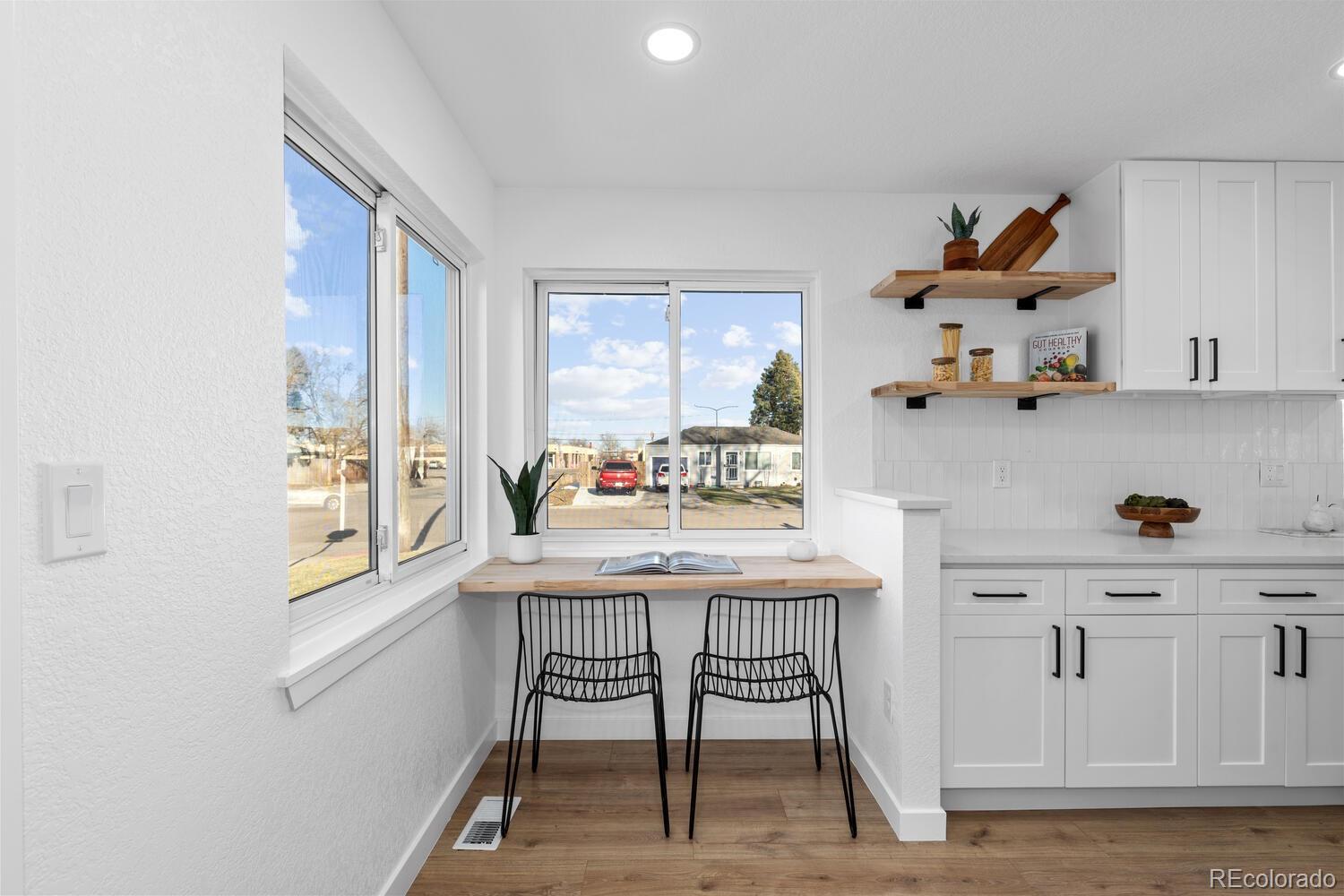 Bright white kitchen with a window-side breakfast counter and two black wire chairs.