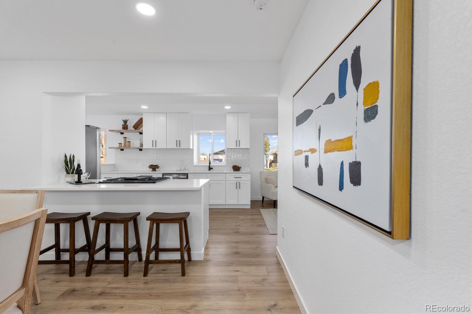 Bright kitchen with white cabinetry, a cooktop island, dark wood stools, and light wood flooring.