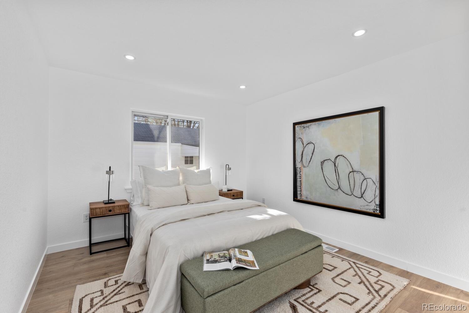 Staged bedroom with a white bed, abstract wall art, and a green bench at its foot.