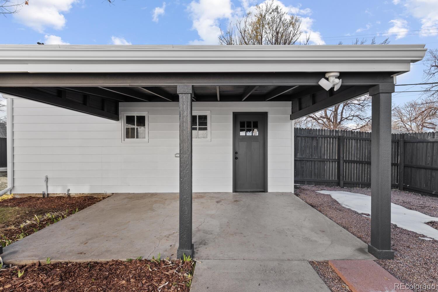 Covered concrete patio with dark support posts and a gray exterior door beside a fenced yard.