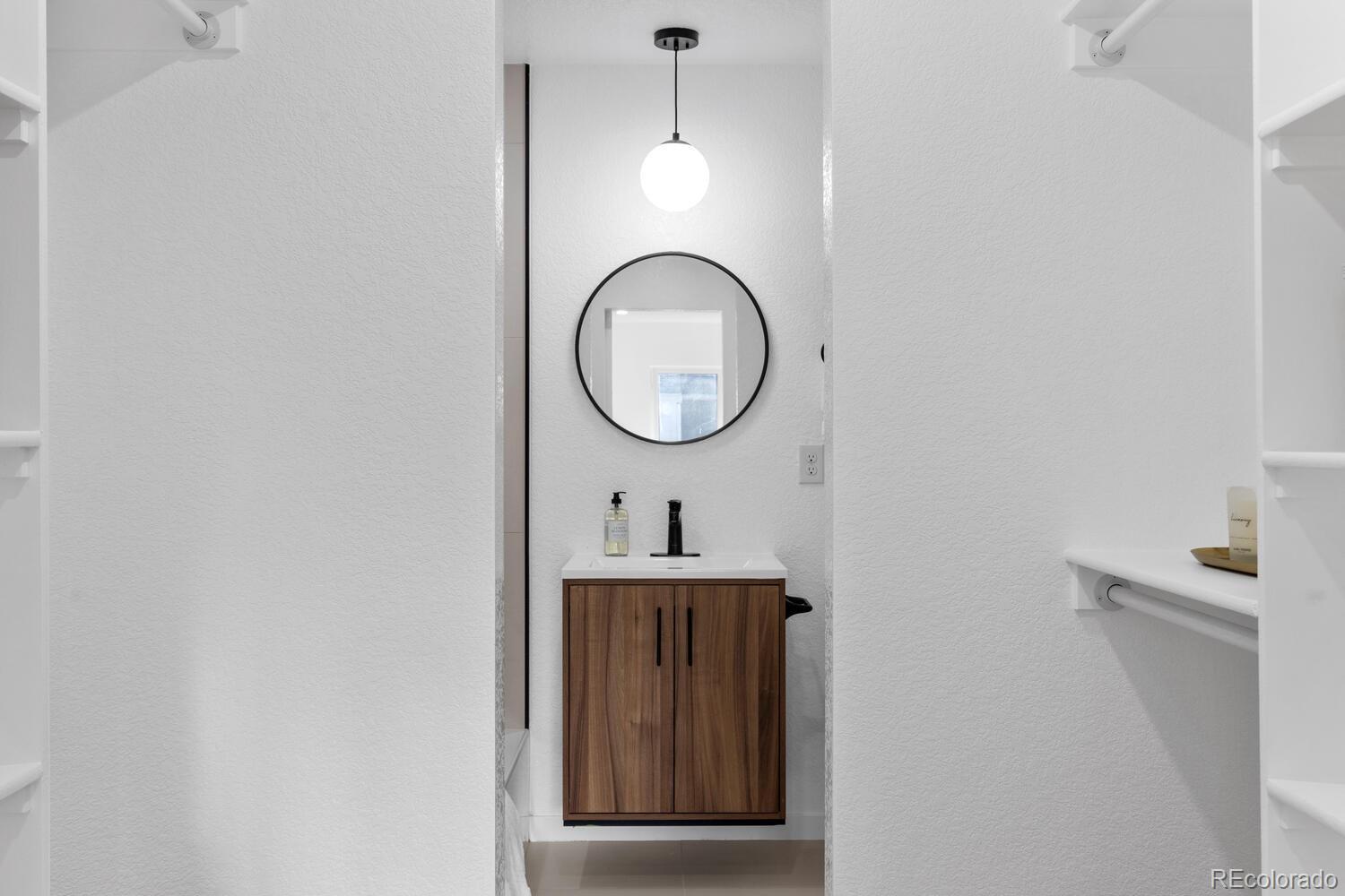 Bathroom vanity with wood-front cabinet, round mirror, and globe pendant light.