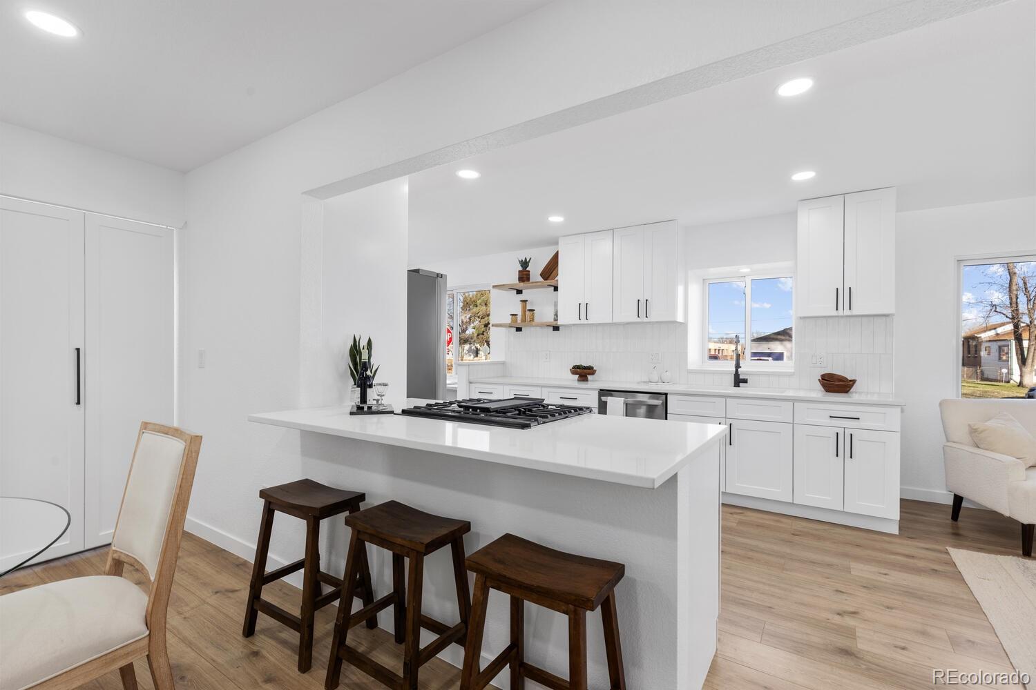 Bright white kitchen with a gas cooktop island, dark wood stools, and light wood flooring.