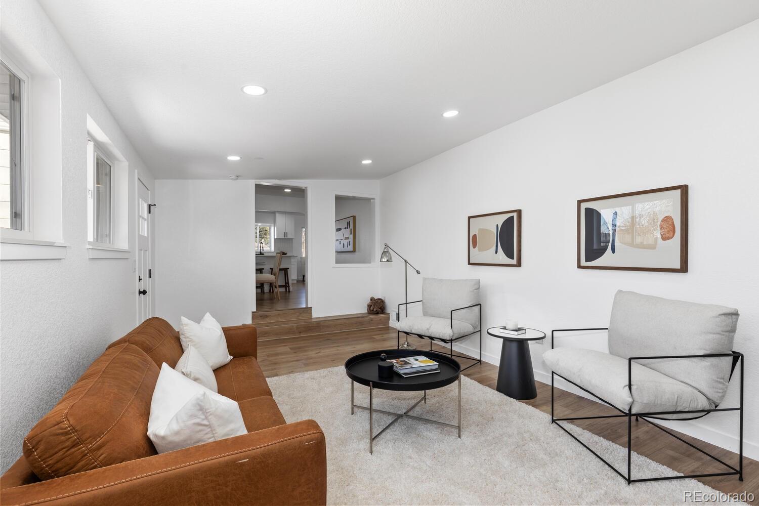 Living room with a caramel leather sofa, white armchairs, and a view into the kitchen.