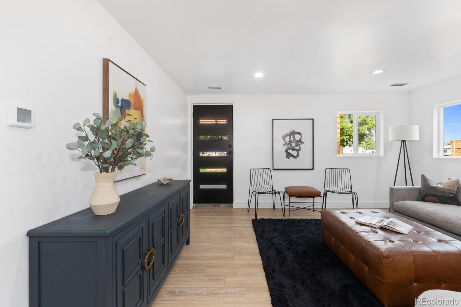 Living room with a black entry door, dark blue sideboard, wire chairs, and brown leather ottoman.