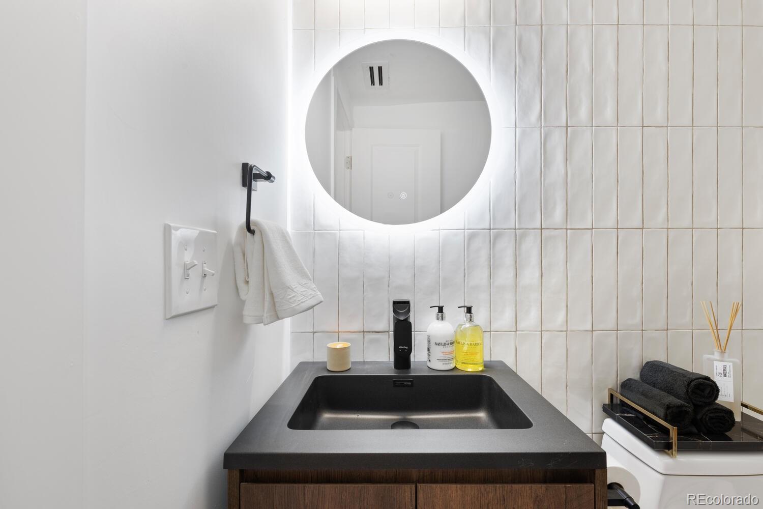 Modern bathroom vanity with a black sink, wood cabinetry, and an illuminated round mirror.