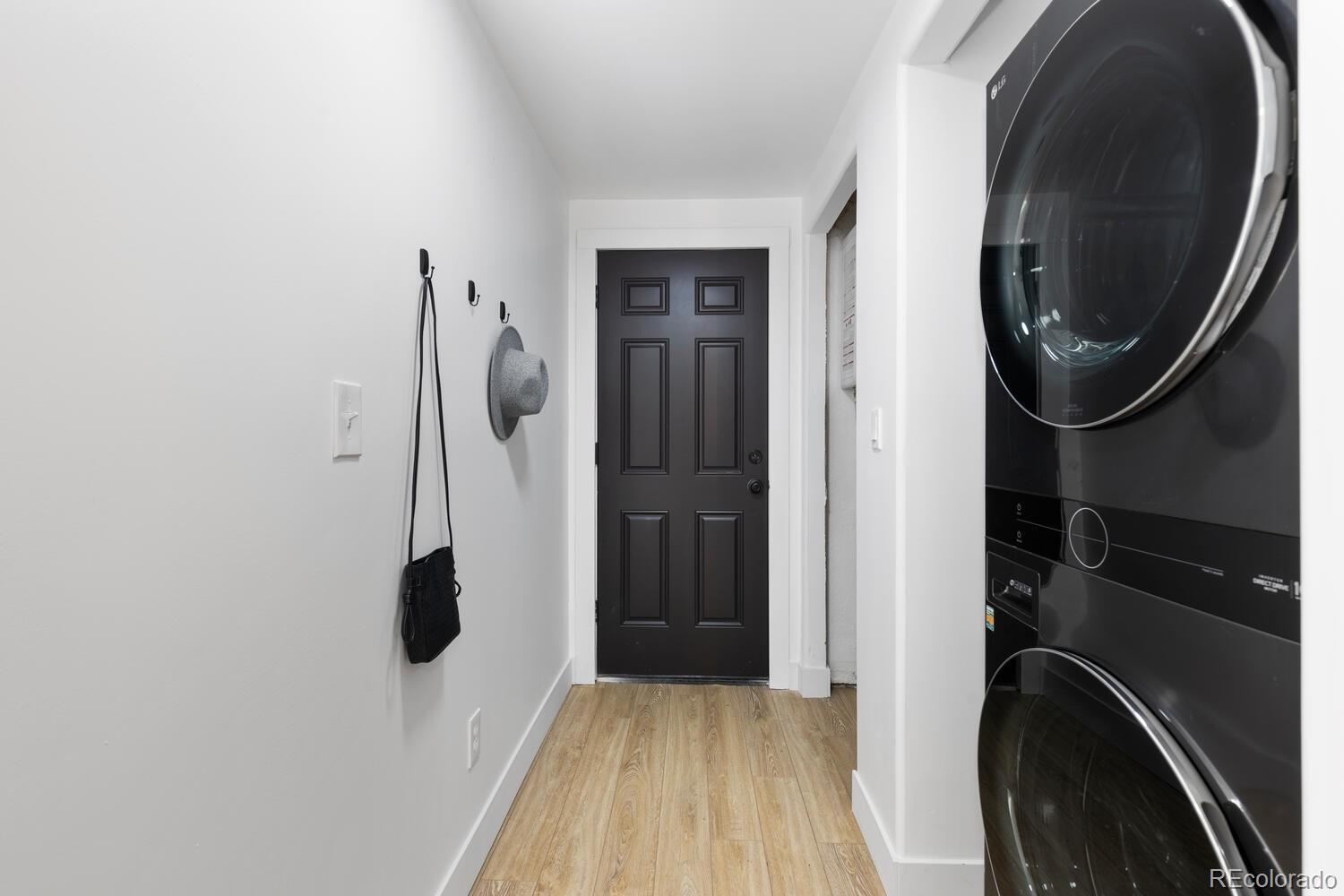 Entry hallway with a black front door, wood-look flooring, and stacked black washer and dryer.