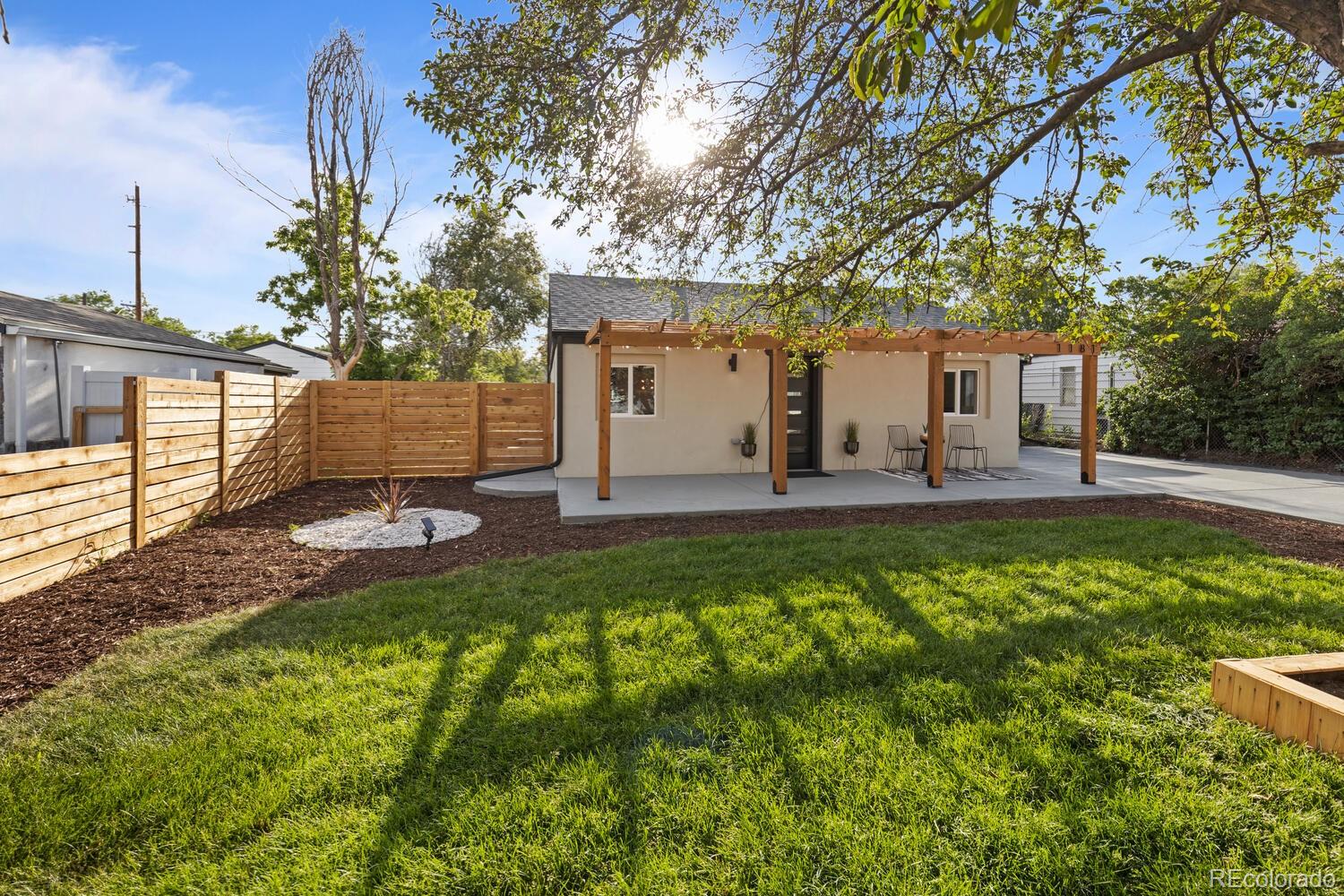Single-story home with a wood pergola-covered patio overlooking a fenced, tree-shaded lawn.