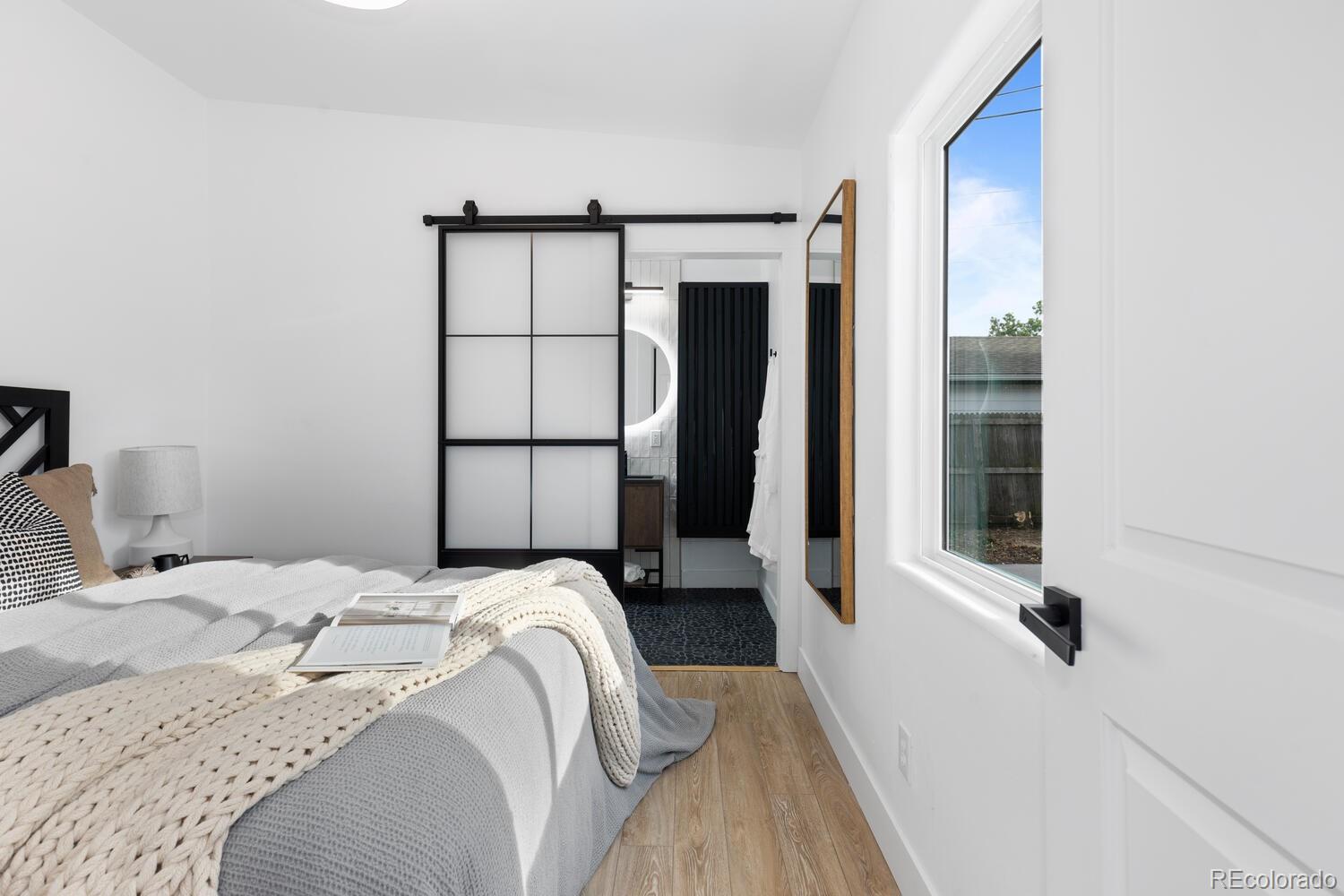 Bright bedroom with a white bed, chunky knit throw, and black-framed sliding door to the bathroom.