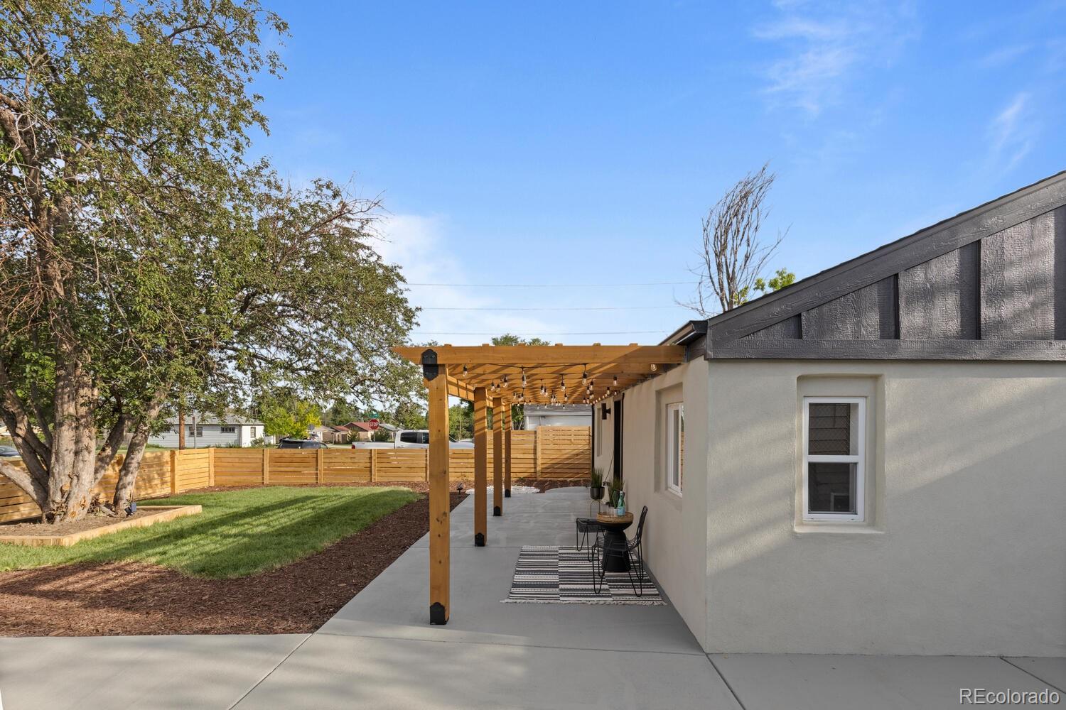 Backyard patio with a wooden pergola, outdoor seating, lawn, and mature trees.