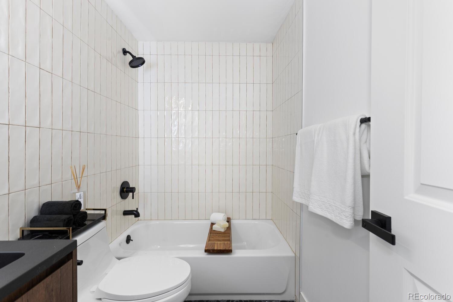 Bathroom with a white tub, vertical tile, black fixtures, and a wooden bath tray.