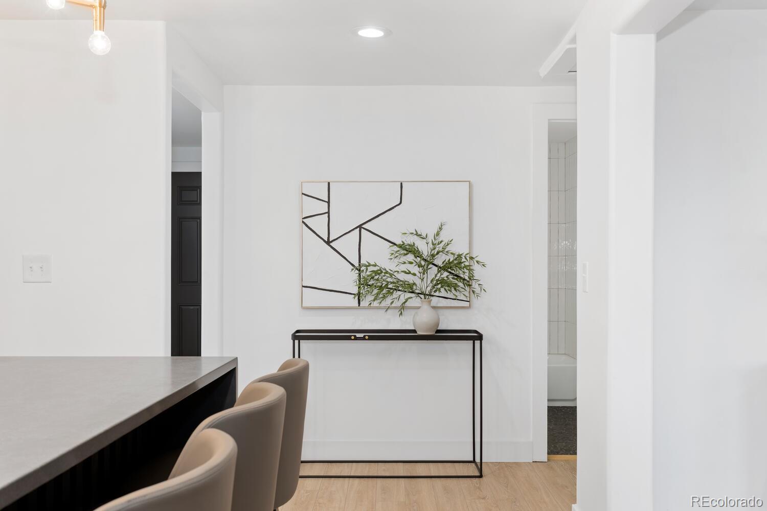 Dining area with a gray island, upholstered stools, and a console table beneath abstract art.