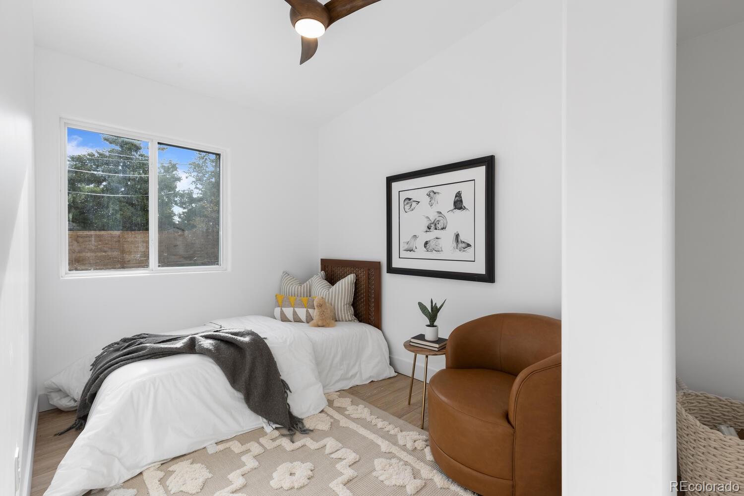 Staged bedroom with a white bed, gray throw, patterned rug, and brown leather armchair.