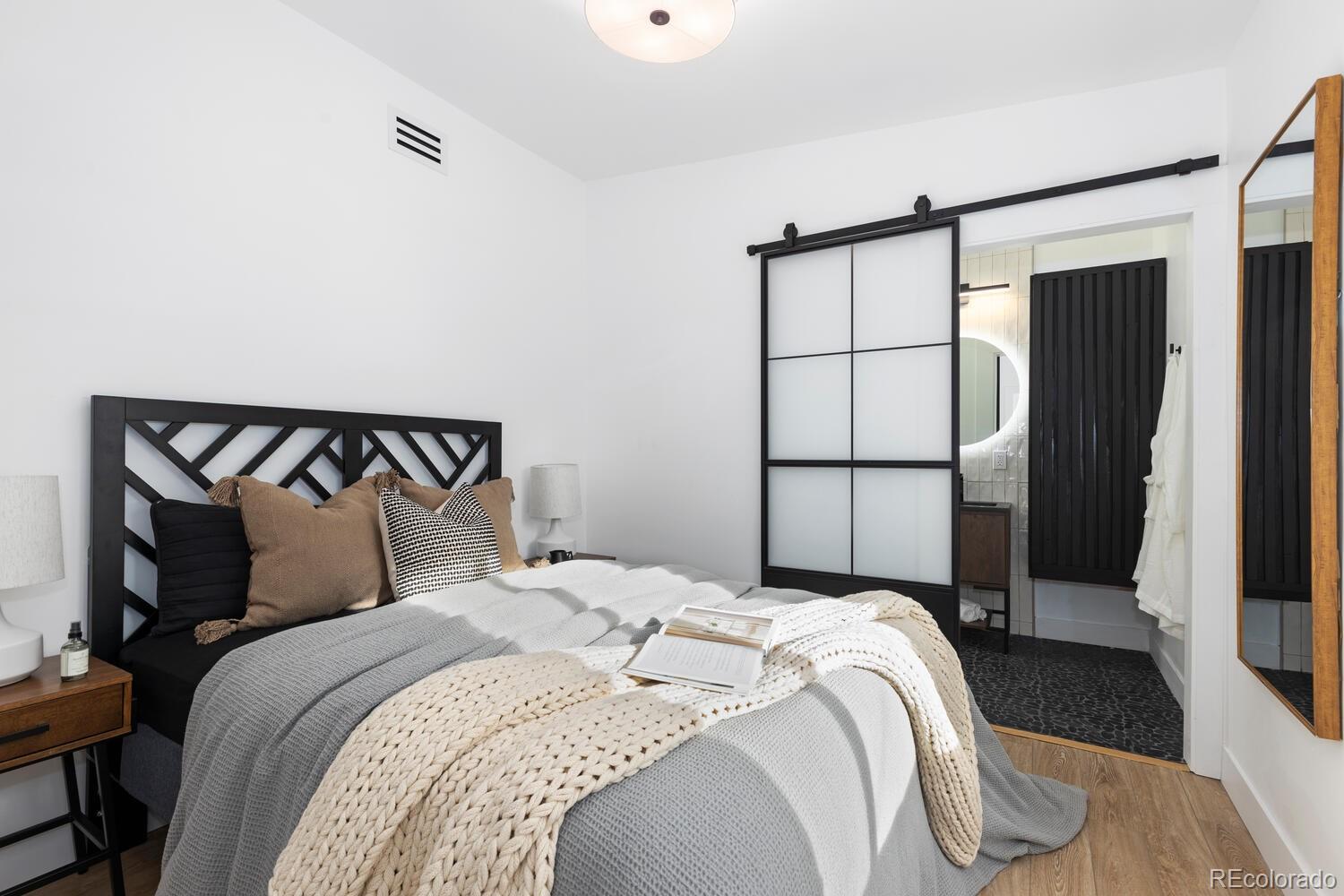 Bedroom with gray and white bedding, a geometric black headboard, and a sliding door to the bathroom.